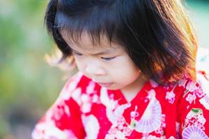 close-up, adorável menina asiática de 1-2 anos está olhando para o caminho dela. um bebê alegre usa um vestido vermelho estilo japonês. durante o verão ou primavera. foto