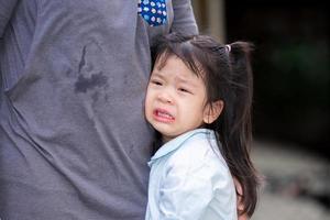 adorável garota asiática está chorando de lágrimas nas bochechas. criança descansou na barriga de sua mãe. crianças está com dor de coração. os de 4 anos usam camisas azuis claras. foto