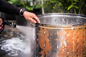 a mão da pessoa que segura a mangueira de água para limpar a sujeira e manchas no tanque de lavagem. ele limpa a parte interna de aço inoxidável para fiação. para reduzir vírus e bactérias. foto