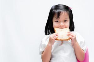 adorável menina saudável segurando um pão branco na frente do rosto. uma criança faminta está prestes a morder um pão. sobre fundo branco.