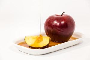 Derramando mel na maçã vermelha e fatia de maçã vermelha no prato branco com mel isolado em um fundo branco foto