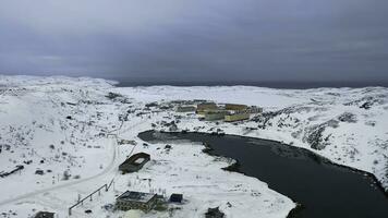 aéreo Visão do uma grandes rio fluindo através a pequeno Vila cercado de Nevado Campos dentro inverno temporada. imagens de vídeo. vôo acima branco prados, edifícios, e calma rio. foto