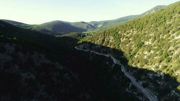 aéreo Visão do a estrada entre Alto montanhas coberto com verde árvores e arbustos contra azul céu dentro ensolarado verão dia. tomada. lindo colorida panorama. foto