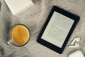 leitor de e-book, uma xícara de café e um fone de ouvido foto