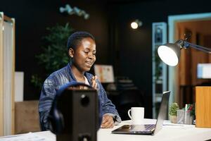 jovem Preto mulher acenando às computador portátil Câmera, atendendo conectados aula, virtual comunicação com colegas. africano americano fêmea trabalhador autonomo vídeo conferência com potencial clientes. foto