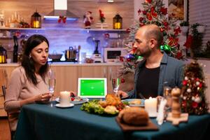 alegre família desfrutando natal jantar dentro x-mas decorado cozinha a comemorar Natal feriado. verde tela zombar acima croma chave tábua computador com isolado exibição em pé em mesa foto