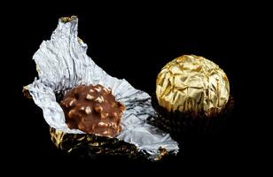 desembrulhado chocolate doce e embrulhado dentro ouro frustrar, em uma Preto fundo. foto