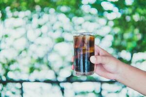 mão segurando uma Coca vidro em uma verde fundo foto