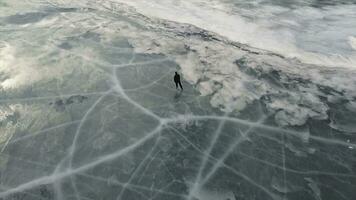 aéreo Visão do uma homem patinação em lago baikal coberto de gelo. grampo. masculino desportista aproveitando esporte dentro frio clima com a céu e nuvens refletido dentro a lindo gelado superfície do a lago. foto