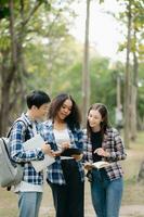 três jovem Faculdade alunos é lendo uma livro enquanto relaxante sentado em Relva dentro uma campus parque com dela amigos. Educação conceito foto