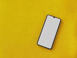 maquete de smartphone móvel preto encontra-se na superfície com uma tela em branco isolada em um fundo de tecido amarelo foto