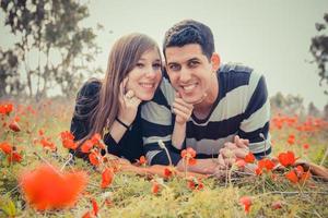 jovem casal deitado na grama em um campo de papoulas vermelhas e sorrindo para a câmera foto