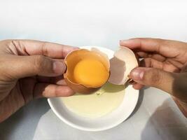 uma mulher mão rachaduras a ovo para separado a ovo branco e gema e a ovo Concha dentro a fundo. foto
