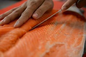 fresco salmão filé fechar-se em branco corte borda mesa enquanto filetagem salmão barriga de chefe de cozinha dentro cozinhando quarto foto