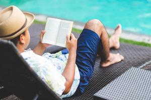 homem lendo livro perto da piscina. relaxe o conceito. foto