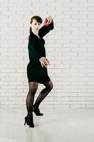 Mulher bonita em um vestido preto, dançando com castanholas vermelhas, fundo de tijolo branco foto