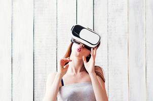 jovem usando óculos VR, com as mãos no rosto, fundo branco de madeira foto