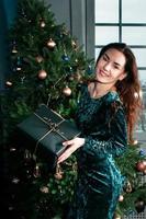 linda garota com caixa de presente sorrindo perto da árvore de natal foto