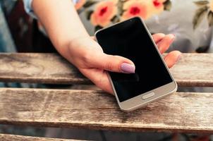 mão feminina segurando um telefone inteligente com tela em branco, na mesa foto