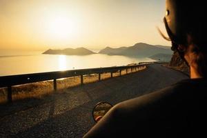 motociclista dirigindo ao longo da estrada da montanha ao pôr do sol sobre o mar, movimento borrado foto