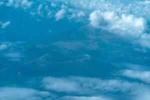 Visão do a terra abaixo enquanto vôo acima a nuvens, montanhoso terreno através atmosférico confusão, Visão a partir de acima foto