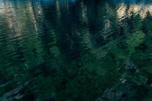ondulado água superfície do uma Claro lago com reflexão do montanhas e madeira foto