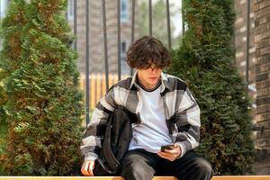 jovem homem digitando alguma coisa em a telefone enquanto sentado dentro a parque foto
