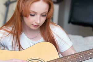 jovem mulher jogando acústico guitarra às lar, retrato fechar-se foto