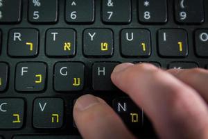 homem digitando em um teclado com letras em hebraico e inglês foto