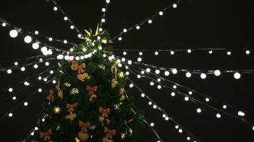 Visão a partir de a inferior em a lindo Natal árvore com colorida decorações e festão do branco luzes em pé em a quadrado. conceito. lindo Nevado inverno cenário do Natal feriado foto