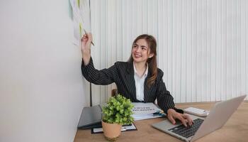 retrato jovem empresária apresentação marketing e lucro com confiante às escritório, investimento e seminário para planejamento do finança, o negócio mulher em pé explicando gráfico e gráfico. foto