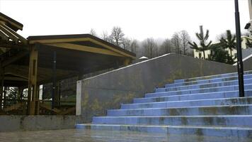 de madeira pavilhão dentro chovendo estação localizado perto concreto escadas em cinzento pesado céu fundo. estoque imagens de vídeo. coberto gazebo debaixo a chuva dentro atrasado outono. foto