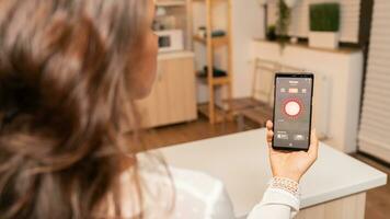 mulher dentro cozinha usando voz controlar em telefone para mudança iluminação. pessoa dentro apartamento segurando Telefone com tela sensível ao toque e aplicativo para luzes. foto