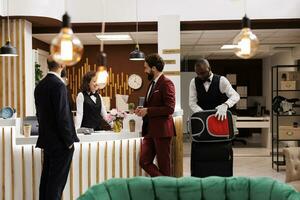 colegas cumprimentado de recepcionista às frente mesa, parceiros dentro ternos A chegar às luxo hotel para comparecer executivo o negócio reunião, viajando para trabalhar. homens em jornada, conferência participação. foto