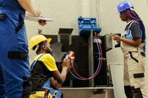 capaz eletricistas habilmente reenchimento Freon dentro ao ar livre ar condicionador enquanto usando múltiplo metros para perfeitamente a medida a pressão dentro hvac sistema, garantindo requeridos resfriamento desempenho foto