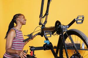 Atlético Preto mulher absorta dentro fixação quebrado bicicleta componentes com especialista ferramentas. africano americano senhora habilmente ajustando, examinando, e reparação bicicleta partes para ótimo desempenho. foto