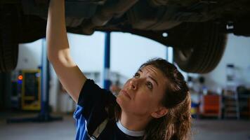 qualificado engenheiro trabalhando em suspenso carro dentro garagem, verificação componentes durante rotina manutenção. auto reparar fazer compras empregado por baixo veículo usando trabalhos luz para Veja para potencial problemas foto