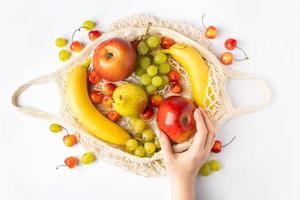 mulher coloca frutas maduras em uma sacola de malha ecológica para fazer compras. mãos femininas seguram um saco de algodão com produtos agrícolas orgânicos. estilo de vida sustentável. foto