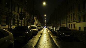 europeu rua dentro luz do amarelo lanternas às noite com carros dentro estacionamento. conceito. em linha reta lindo rua com residencial edifícios e estacionado carros aceso de amarelo lanternas às noite foto