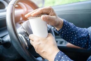 senhora asiática segurando a comida do copo de café para beber no carro, perigoso e risco de um acidente.