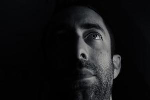retrato dramático de um jovem com metade do rosto inexpressivo na sombra profunda, olhando para cima isolado no fundo preto foto