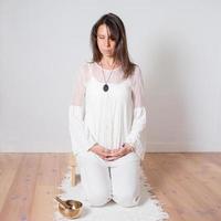mulher adulta caucasiana vestida de branco durante uma sessão de meditação. gongo de metal próximo a ela. foto
