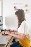 mulher atraente, trabalhando em casa. mesa de madeira e cadeira ergonômica ajoelhada foto