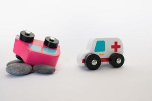 ambulância chegando para ajudar após um acidente de carro. veículos de madeira de brinquedo, um carro rosa e uma ambulância com fundo branco foto