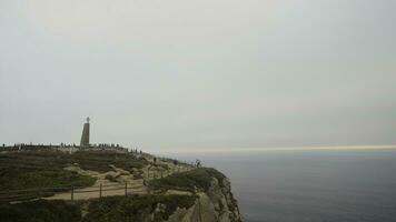 Portugal, Lisboa - Julho 29, 2022. capa com turistas e Cruz. Ação. memorial Cruz às penhasco com mar. uma muitos do turistas às capa Rocha com monumento em nublado dia foto