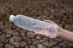feche a mão de uma mulher segurando a garrafa de plástico transparente no fundo do solo de rachadura foto
