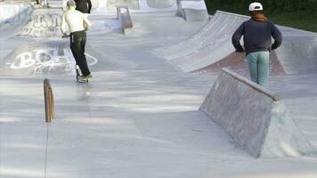 jovem adolescentes equitação patinetes e fazendo truques às a patim parque. meios de comunicação. jovem rapazes gastar Tempo ao ar livre dentro a horário de verão e equitação patinetes. foto