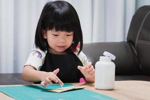 menina doce criança aplicando pedaços de caixas de papelão usando cola enquanto fazia artes e ofícios na aula de aula na escola. artesanato para crianças. projeto de criatividade infantil. trabalhos manuais. foto