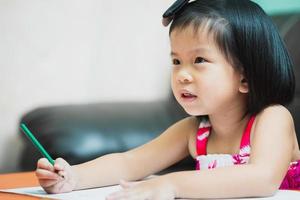 aluna feliz fazendo lição de casa de arte. criança segurando a cor de madeira verde na mão direita. criança positiva aprendendo em casa. foto