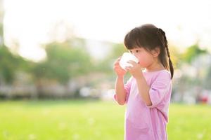 adorável criança asiática está bebendo água doce em copos de plástico. fundo verde natural. no verão ou na primavera. vista lateral da criança é de 4 anos de idade vestindo uma camisa rosa com sede. foto